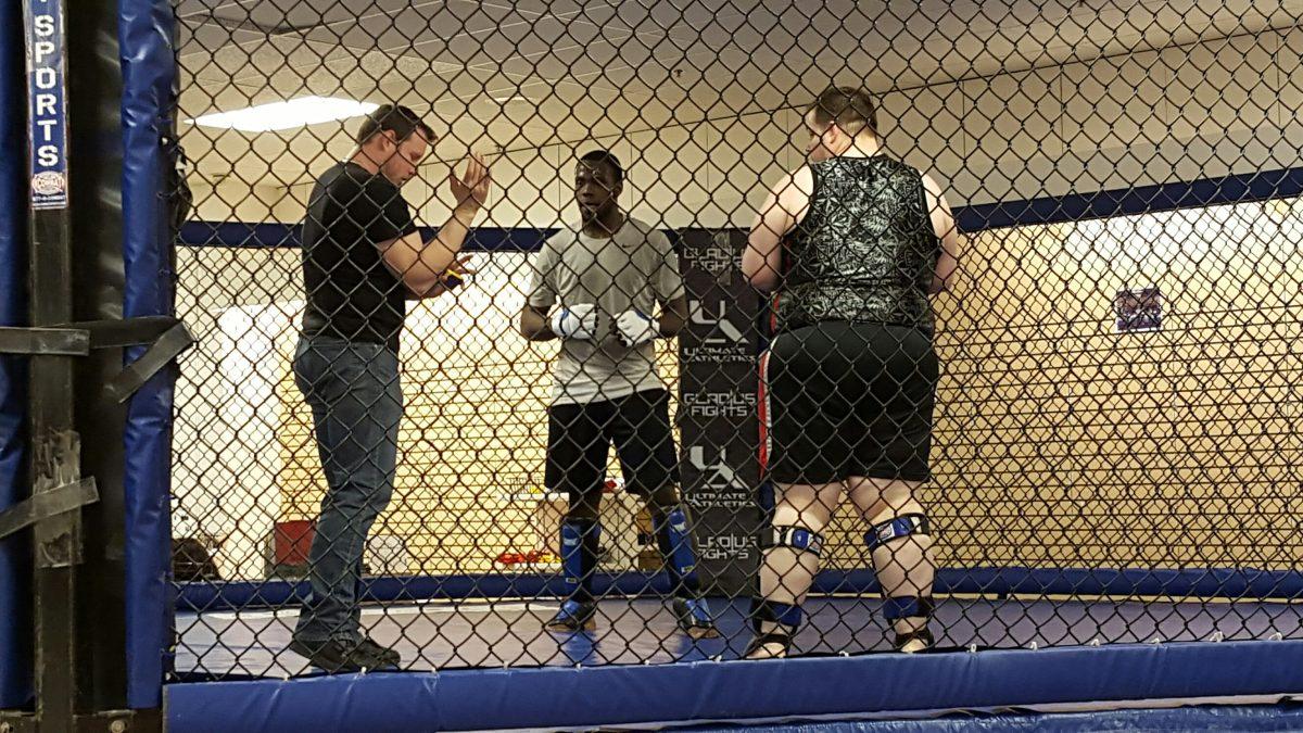 Armus Guyton, center, listens to an instructor while fighting an opponent in the cage on April 1 at the Ultimate Athletics gym.