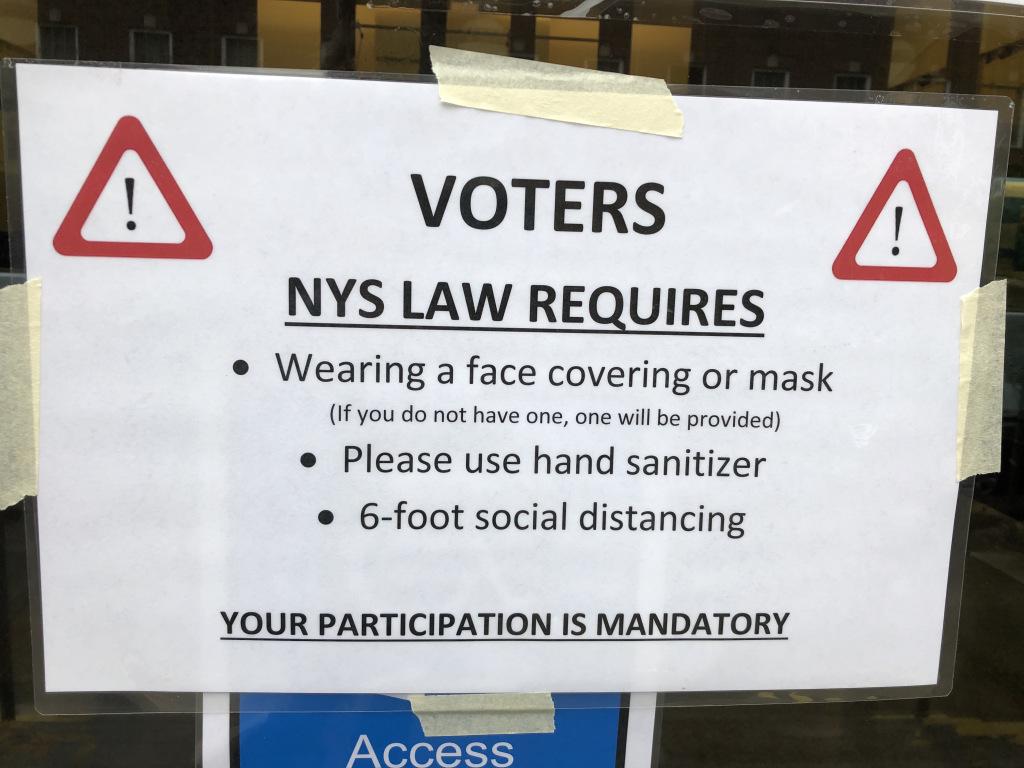 Sign stating voters are required to wear a face mask, use hand sanitizer, and social distance 6 feet apart.