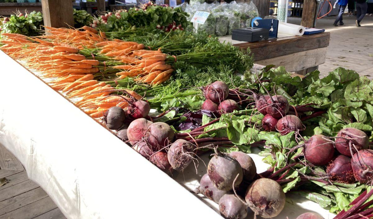 A table at the farmers market is covered with vegetables, including carrots, beets and radishes.