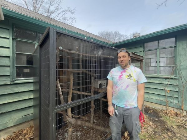 a man stands in front of an animal enclosure with a squirrel in it.
