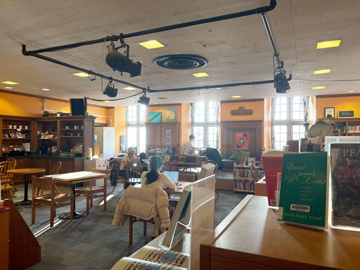 An establishing shot of the Durland Alternatives Library with people sitting at tables and chairs, bookshelves filled with books and walls with art.